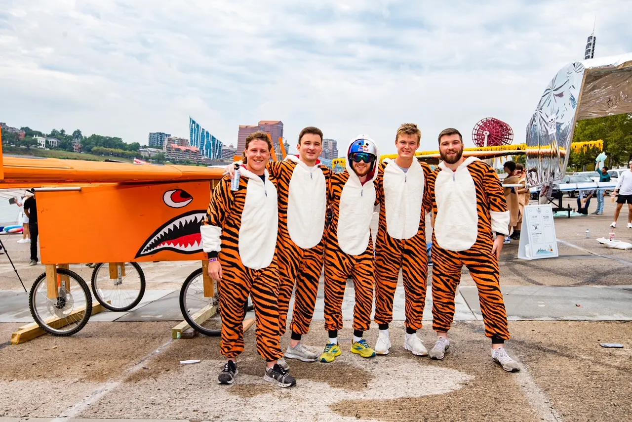 The five team members in tiger costumes standing in front of the glider.