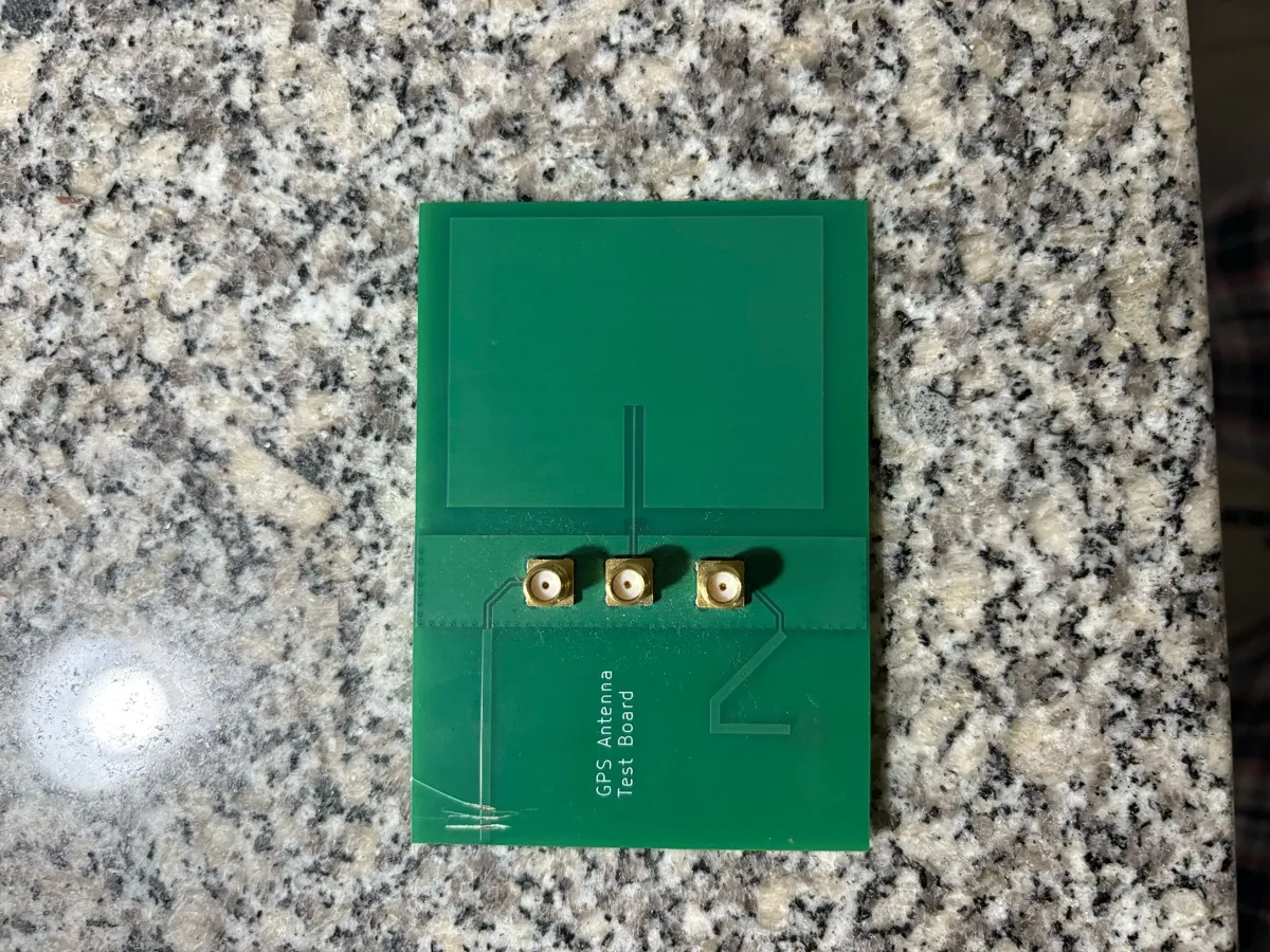 Green antenna test coupon PCB with three SMA connectors, lying on a granite countertop.