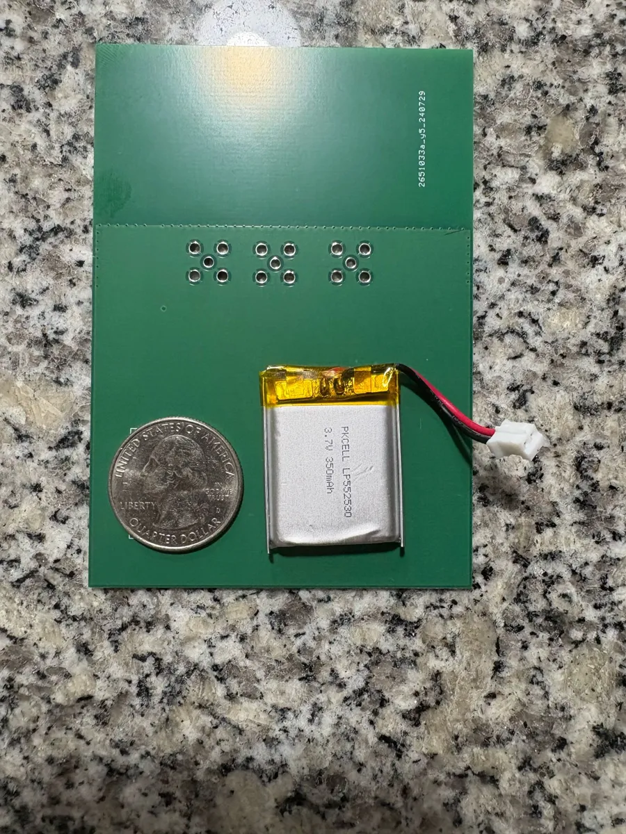 Small silver LiPo pouch battery next to a US quarter on a green PCB, for scale.