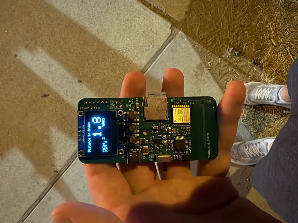 Range finder board held in an open palm outdoors, with the OLED screen lit.