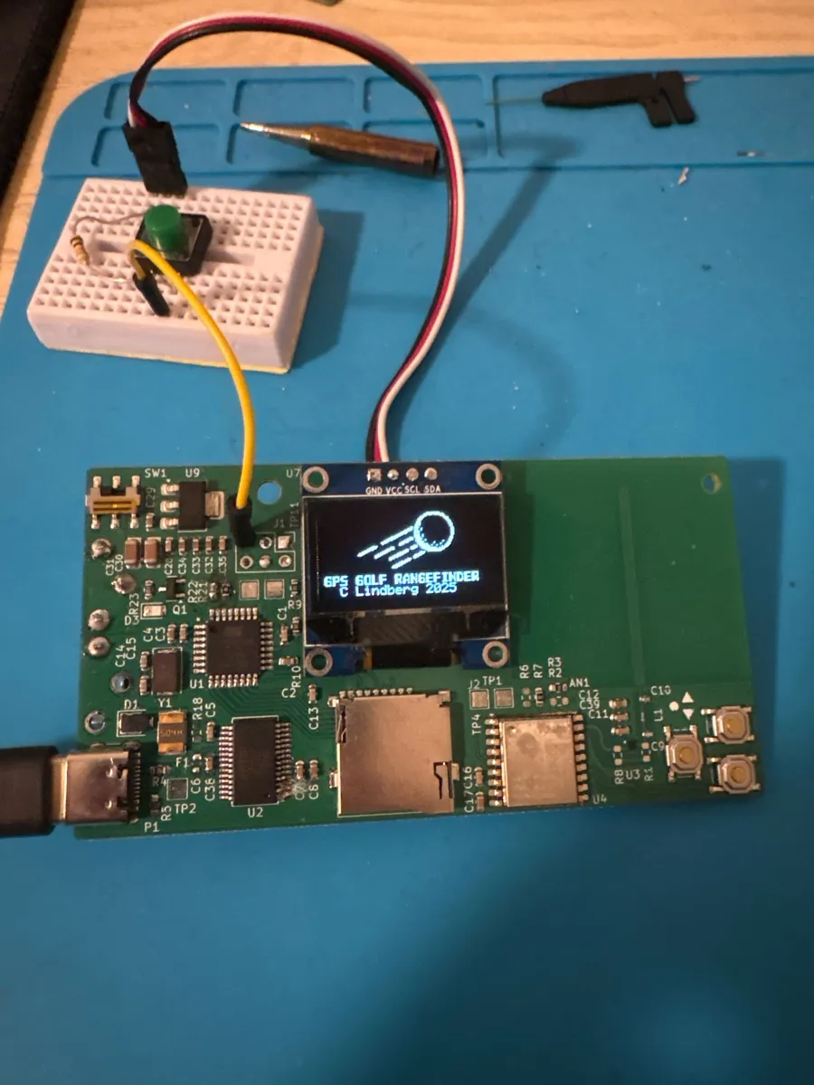 Rev 1 green PCB with an OLED screen connected by jumper wires to a breadboard.